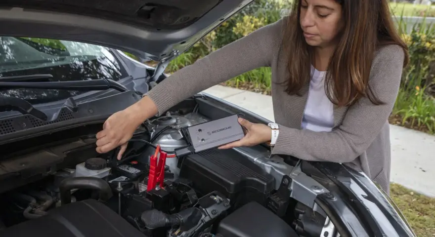 Woman connects a jump starter to a car battery. She's learning how to reset my jump starter.