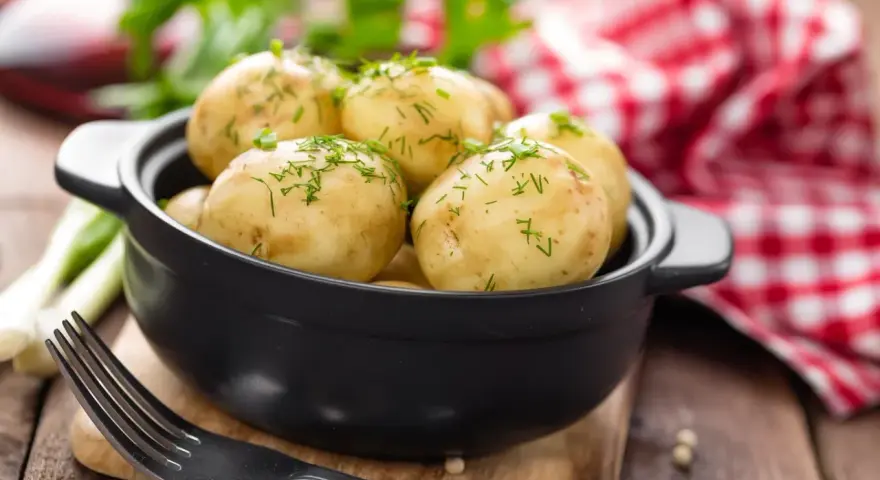 Gotujesz ziemniaki na ból ucha? Te młode ziemniaczki, posypane koperkiem, wyglądają apetycznie. Obok widelec i czerwono-biała serwetka.