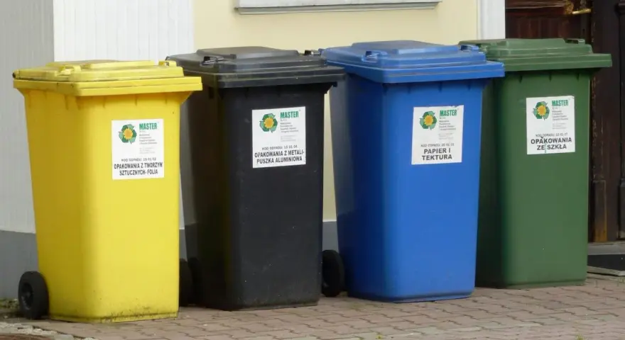 Cztery kolorowe kosze na śmieci: żółty na folię, czarny na metale, niebieski na papier i zielony na szkło. Różne rodzaje koszy ułatwiają segregację.