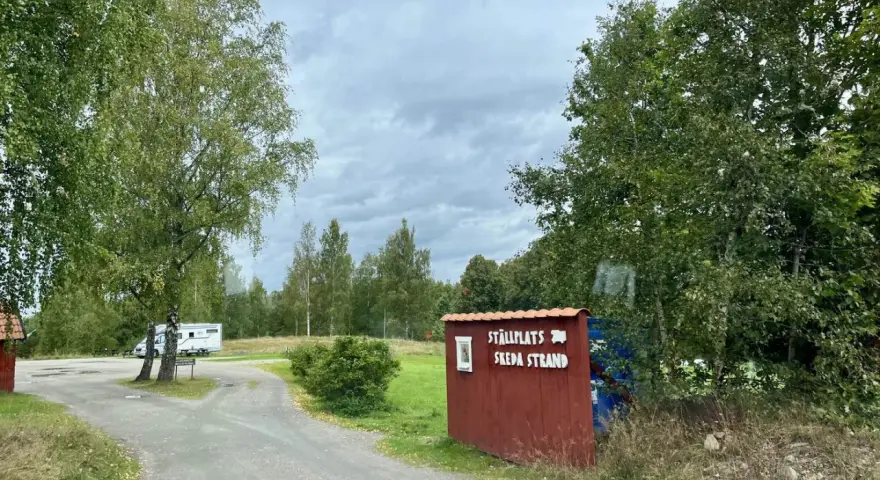 Välkommen till ställplatsen vid Skeda strand. En husbil står parkerad bland träden.
