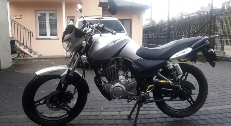 Srebrny Zipp Manic 125 na brukowanym podwórku, gotowy do jazdy.