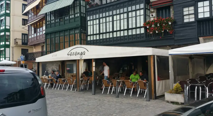 Gente disfrutando de una comida en Lekeitio, sentados en mesas al aire libre bajo un toldo blanco.