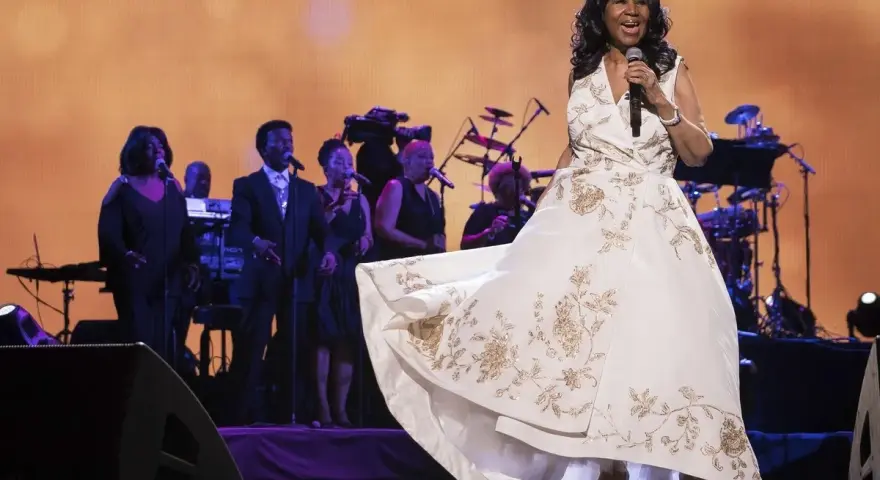 Aretha Franklin w białej sukni z haftem, śpiewa na scenie z chórem. Jej dzieci z pewnością byłyby dumne.