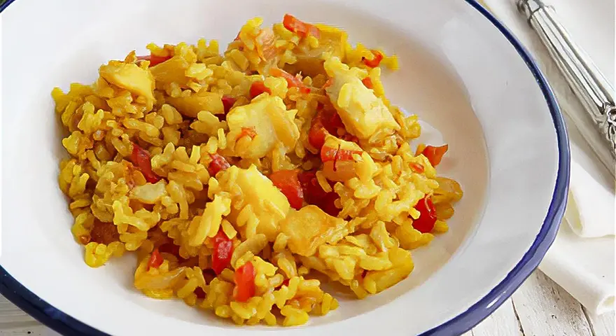 Arroz amarillo con trozos de bacalao y pimientos rojos en un plato blanco.