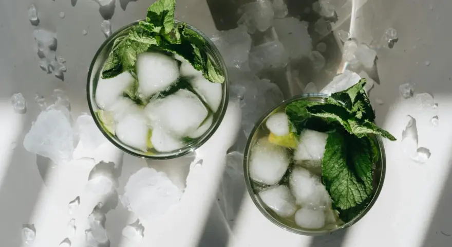 Dwa orzeźwiające mojito z lodem i miętą, otoczone pokruszonym lodem, w letnim słońcu.