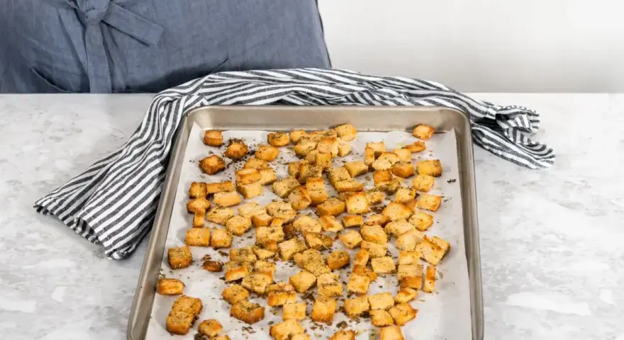 Una teglia piena di crostini di pane dorati e croccanti, conditi con erbe aromatiche. Perfetti per insalate o zuppe.