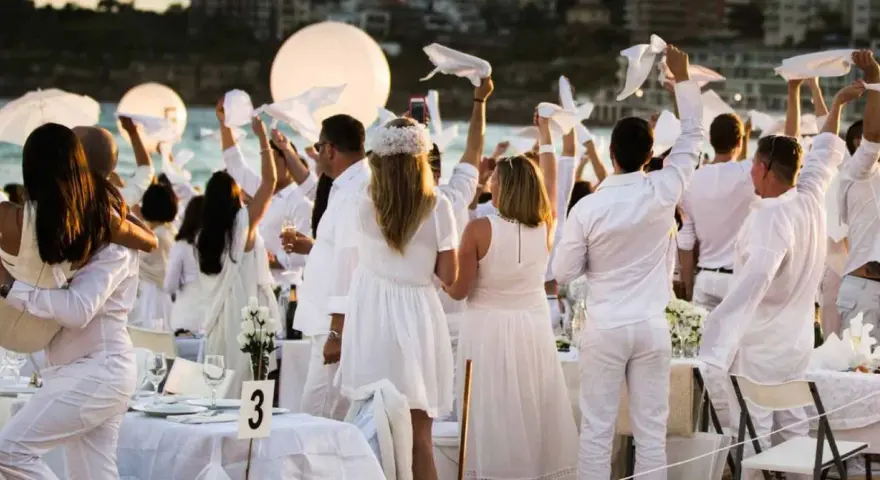 Festa in bianco: tutti vestiti di bianco per un evento elegante sulla spiaggia. Un'atmosfera magica con palloncini luminosi e tavoli apparecchiati.