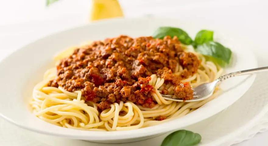 Ein Teller Spaghetti mit einer reichhaltigen, traditionell zubereiteten Bolognese-Sauce, garniert mit frischem Basilikum.