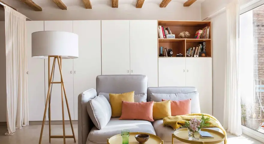 Sofá gris con cojines coloridos, mesa auxiliar amarilla y lámpara de pie. Ideas para decorar piso alquiler low cost con estilo y calidez.