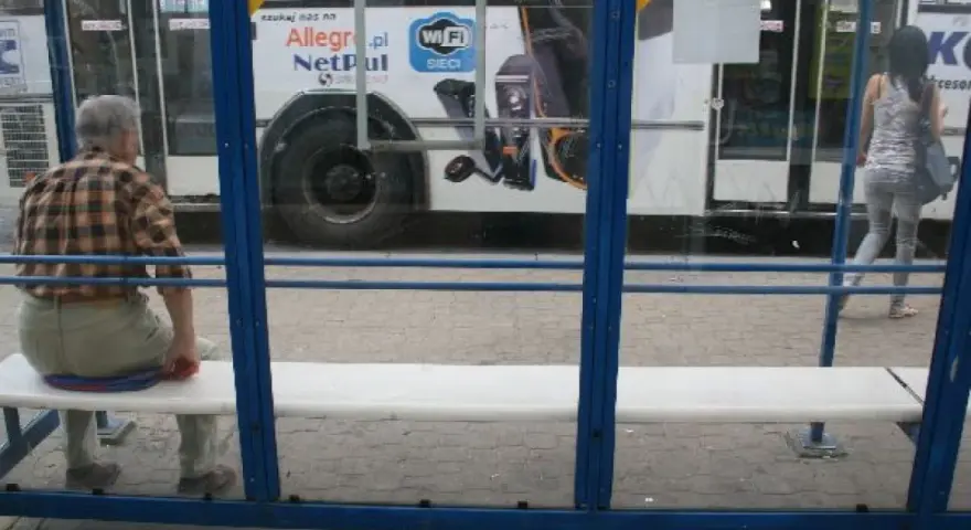 Mężczyzna czeka na przystanku na autobus 102. Rozkład jazdy jest niewidoczny, ale widać autobus z reklamą Allegro.