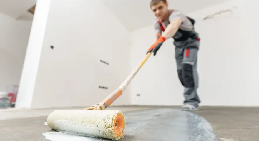 Man målar garagegolv med en roller.