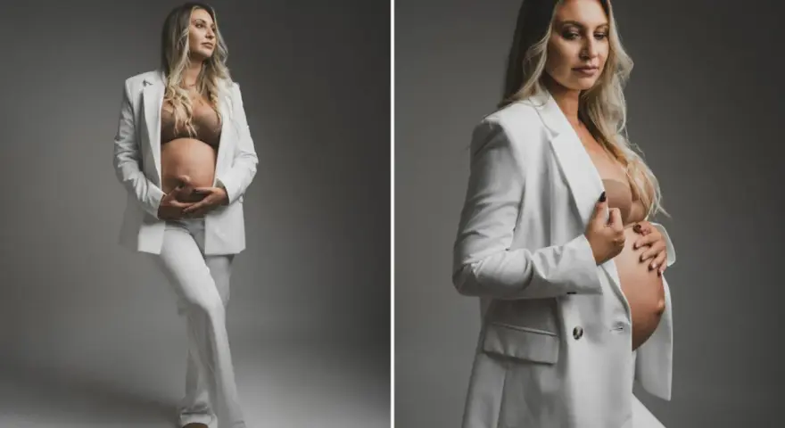 Elegancka kobieta w białym garniturze podczas sesji ciążowej, czule trzymająca się za brzuch.
