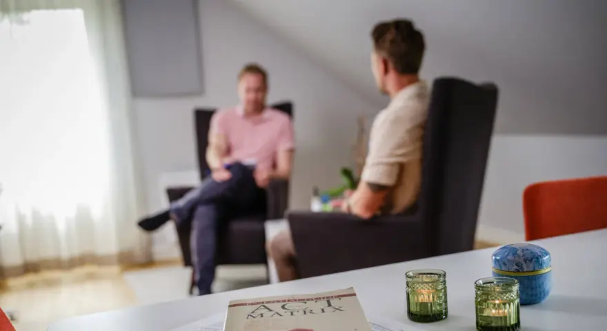 Två män i samtal i en lugn miljö. En bok om acceptance and commitment therapy svenska ligger på bordet.