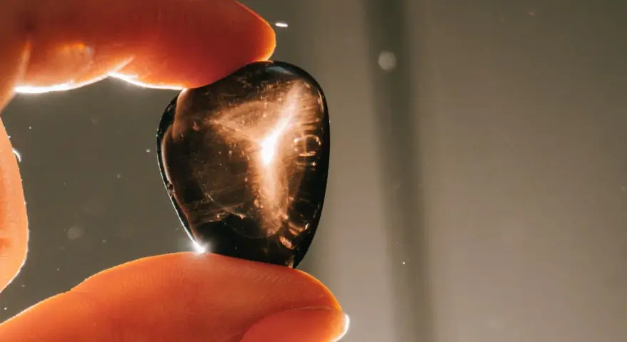 Dedos sostienen una piedra oscura con destellos dorados. ¿Qué pasa si se rompe una piedra energética? Quizás solo se dispersa su luz.
