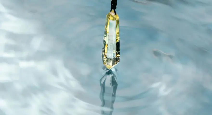 Un cristal de selenita cuelga sobre agua azul, reflejando su brillo. Quizás es porque la selenita necesita agua para purificarse.