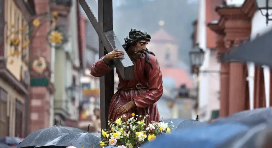Prozession am Karfreitag: Jesus trägt das Kreuz. Gläubige mit Regenschirmen gedenken.