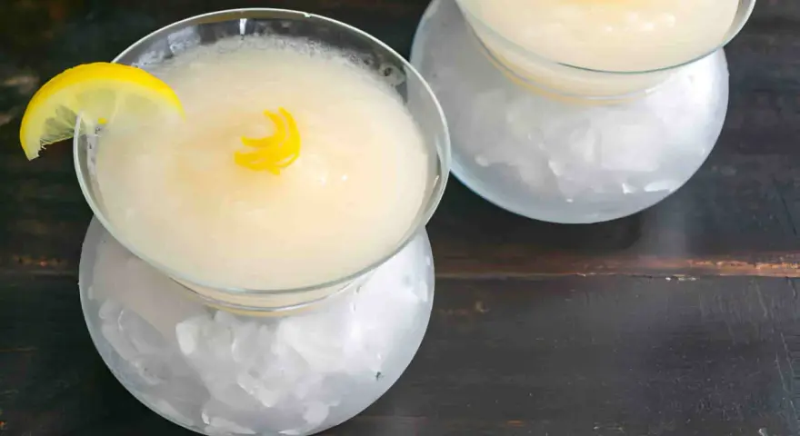 Dos copas de sorbete de limón, una con rodaja de limón y rizo de cáscara, servidas sobre hielo picado.