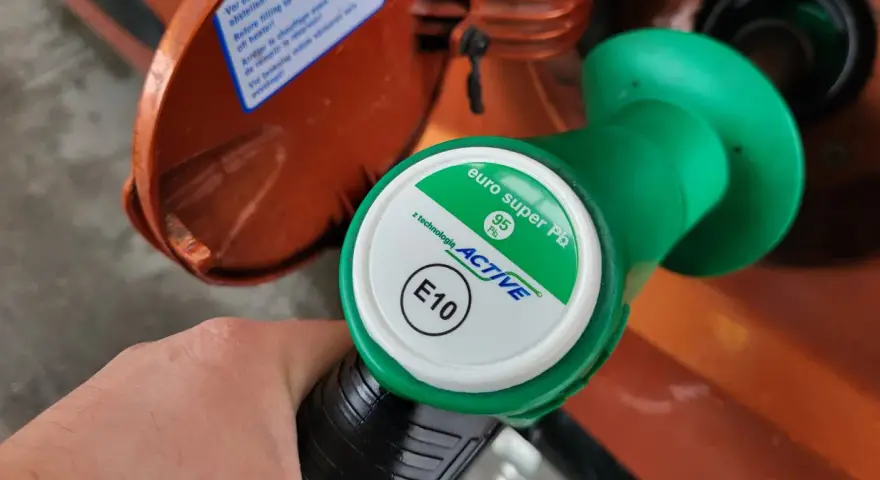 Dłoń trzyma zielony pistolet dystrybutora z napisem "euro super Pb 95 ACTIVE E10". To benzyna e10.