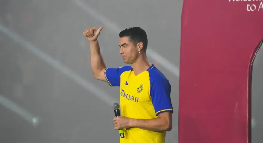 Cristiano Ronaldo w koszulce Al Nassr z mikrofonem, pokazuje kciuk w górę.