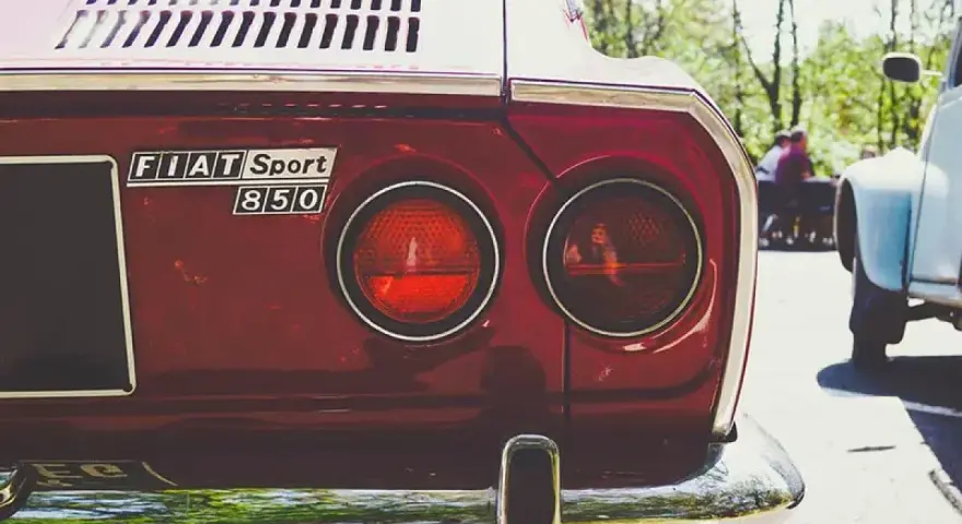 Dettaglio posteriore di una Fiat Sport 850 rossa, con i suoi iconici fanali rotondi. Un pezzo di storia automobilistica, un vero art 102 cds.