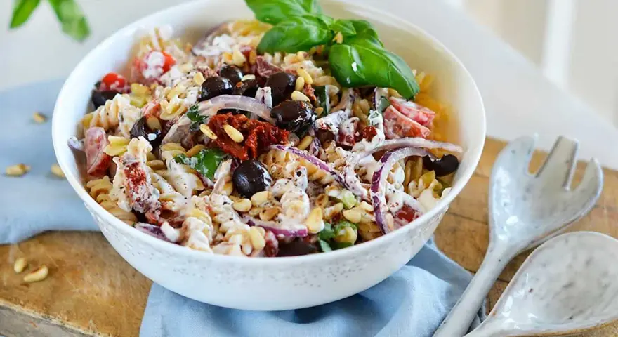 En härlig italiensk pastasallad med rotfrukter, oliver, soltorkade tomater och pinjenötter, toppad med färsk basilika.