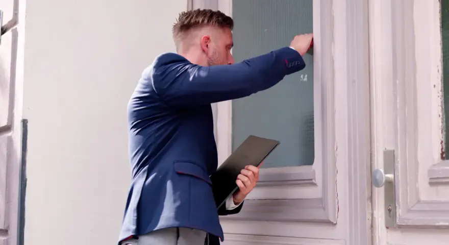 Mężczyzna w garniturze puka do drzwi, trzymając teczkę. Może to być wizyta związana z vex windykacja.