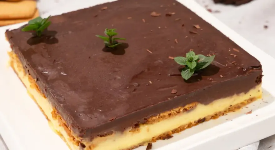 Deliciosa tarta de la abuela con capas de galleta y crema, cubierta de chocolate y decorada con menta fresca.