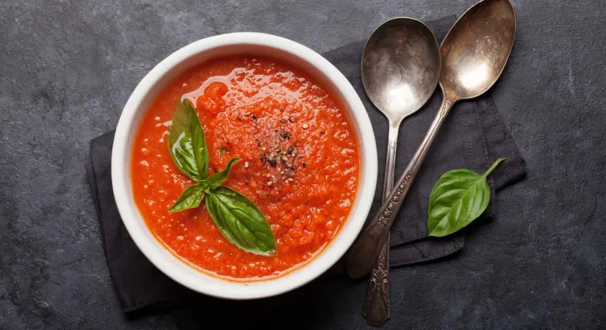 Eine Schüssel mit leckerer, italienischer Tomatensauce, garniert mit Basilikum und Pfeffer. Daneben liegen zwei Löffel.