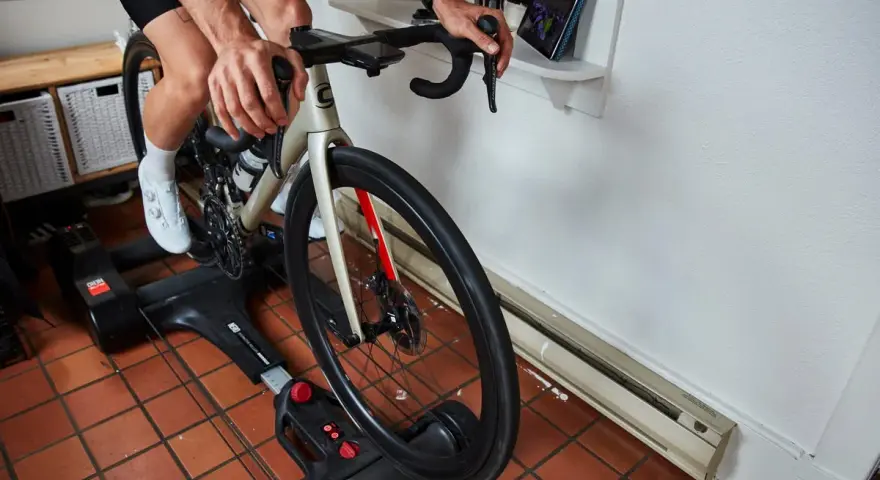 Cyclist on bike rollers, a dynamic alternative to a trainer, rides indoors while watching a tablet.