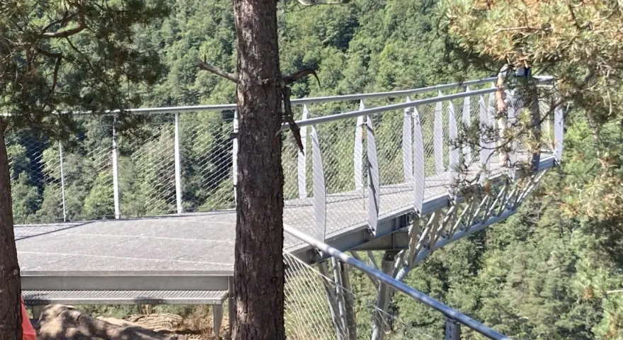 La passerelle himalayenne de Grazac offre une vue imprenable sur la vallée verdoyante. Une personne marche sur la structure métallique.