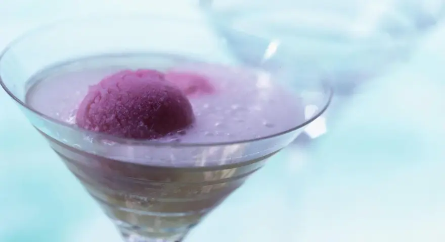 Ein erfrischendes Eis mit Sekt in einem Martiniglas. Die pinke Eiskugel schwimmt in prickelndem Sekt, ein Genuss für heiße Tage.