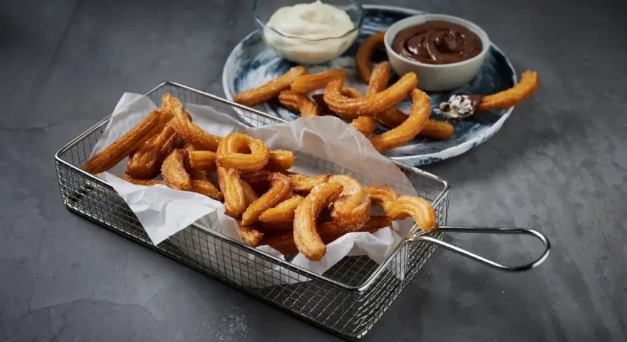 Krispiga churros i korg med chokladsås och grädde. Perfekt för ett enkelt churros recept hemma.