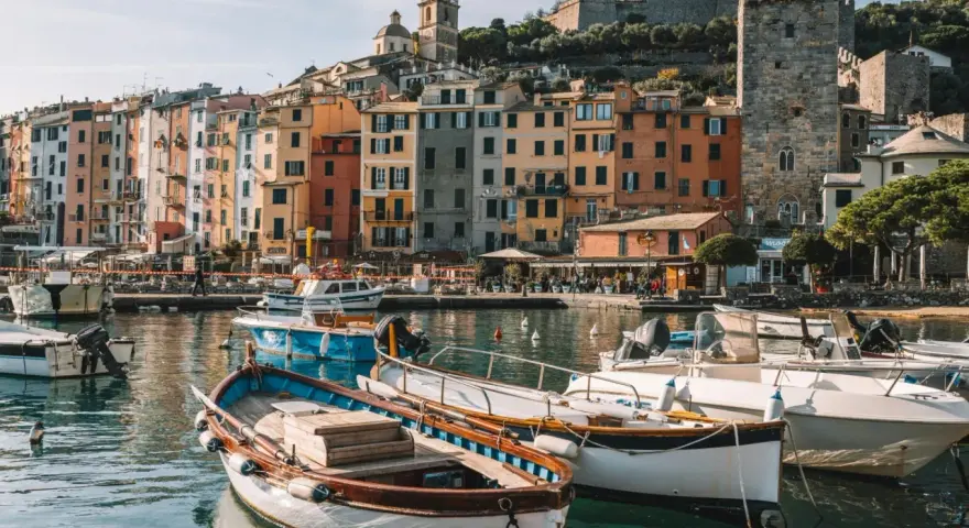 Boats bob in the harbor of a colorful Italian Riviera town, with ancient castles overlooking the vibrant buildings.
