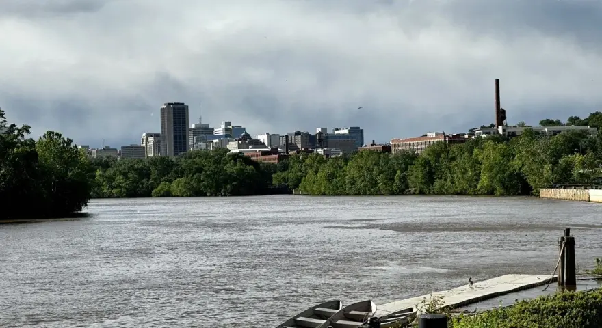 A cloudy sky looms over the Richmond, VA skyline, with the James River in the foreground. This view hints at fun things to do in Richmond, VA, like kayaking or enjoying the riverfront.