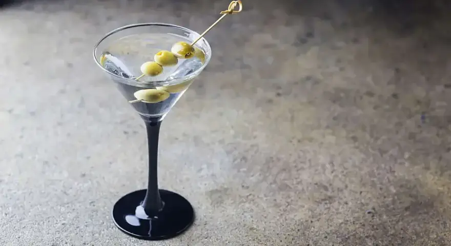 Klasyczny Dirty Martini przepis. Elegancki kieliszek z drinkiem i oliwkami na wykałaczce, gotowy do degustacji.