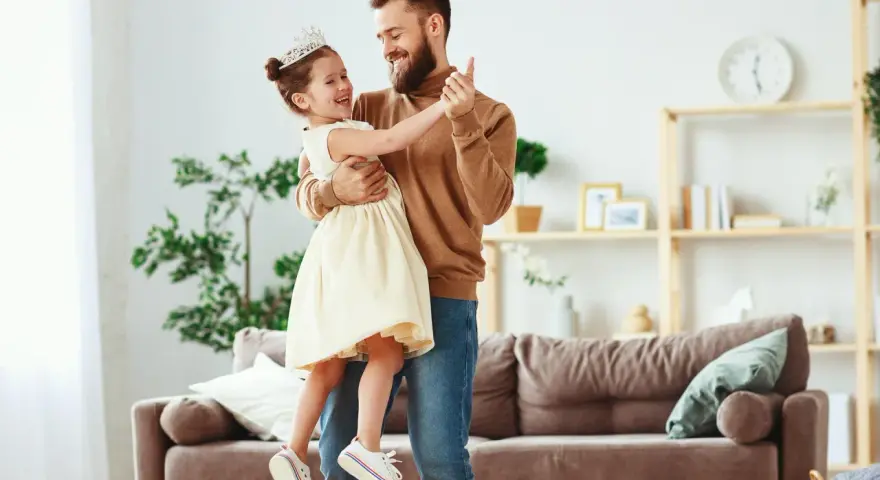 Ojciec tańczy z córką w koronie. Widać ich radość i miłość ojca do córki.