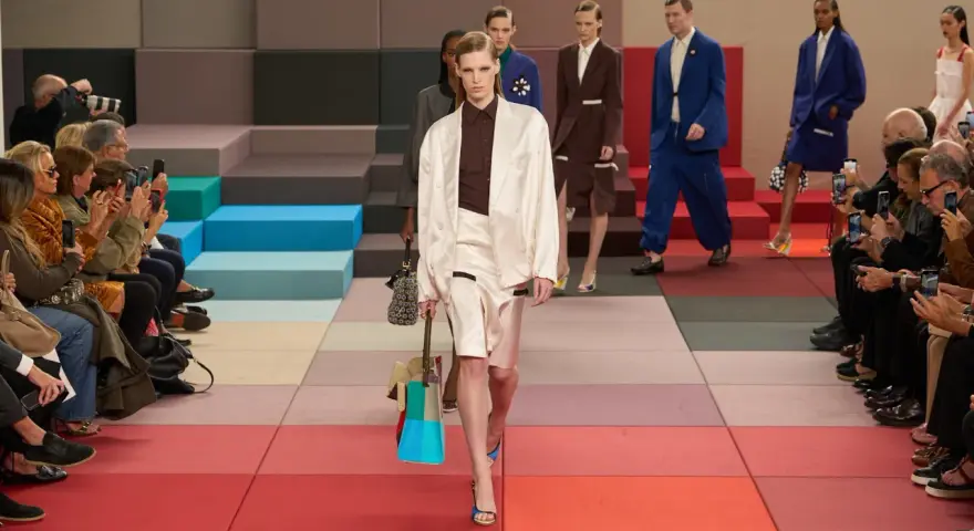 Modella sfila in passerella, un'icona di stile che scrive la sua **fendissime storia**. Pubblico con smartphone documenta l'evento.