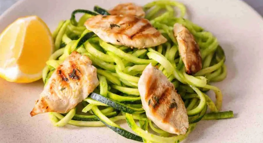 Spaghetti di zucchine con straccetti di pollo grigliato e una fetta di limone.