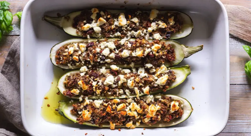 Ugnsbakade zucchinihalvor fyllda med en smakrik blandning och toppade med smulad fetaost. En härlig rätt med zucchini i ugn med fetaost.