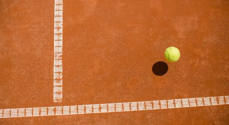 Piłka tenisowa na ceglanej nawierzchni, tuż obok linii bocznej. Czy to decydujący punkt za Roland Garros?