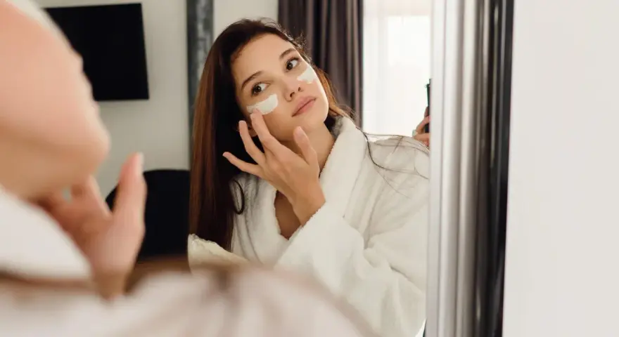 Kobieta w szlafroku nakłada krem pod oczy. Czy retinol to kwas? To pytanie nurtuje wiele osób dbających o cerę.