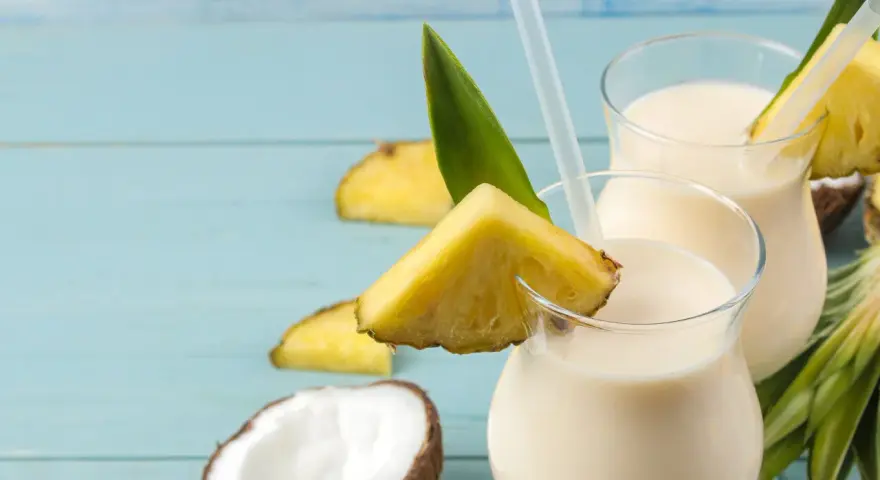 Dwa orzeźwiające koktajle pina colada z kawałkami ananasa i kokosem na niebieskim tle.
