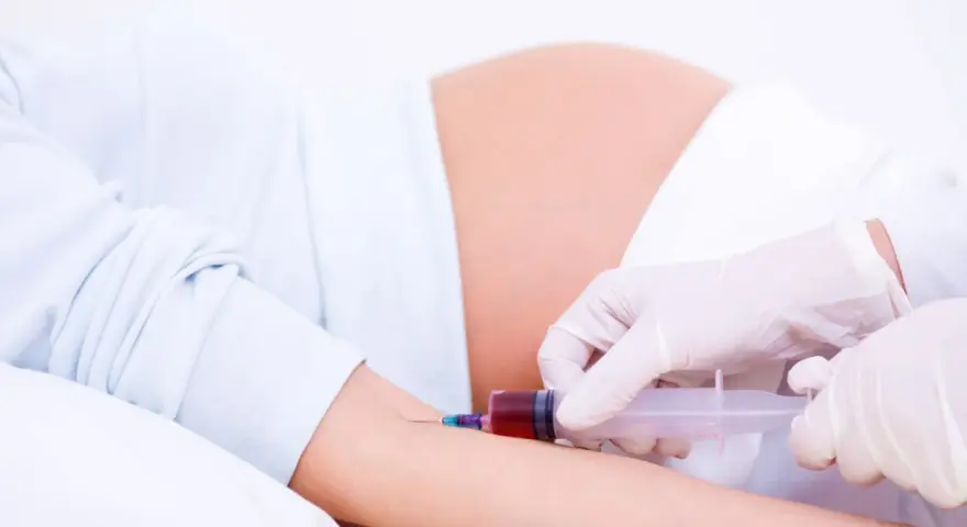 Pobieranie krwi do badań w 15 tygodniu ciąży. Lekarz w rękawiczkach pobiera krew strzykawką od ciężarnej.