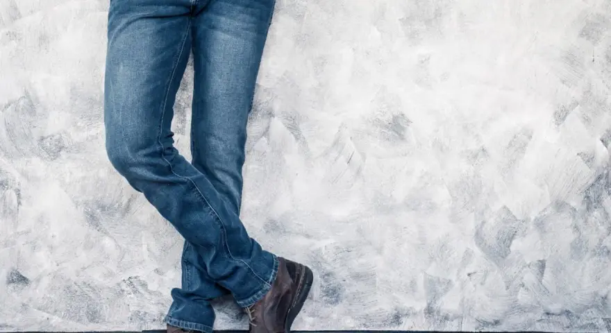 Mężczyzna w jeansach H&M, stojący przy ścianie. Rozmiarówka H&M wypada standardowo, idealnie dopasowana.