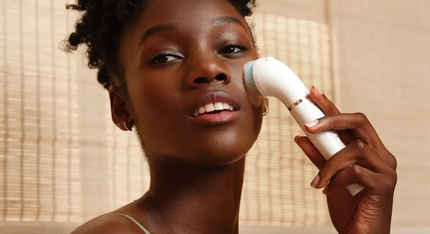 Donna con pelle scura usa un dispositivo per un trattamento esfoliante viso, per una pelle luminosa e pulita.