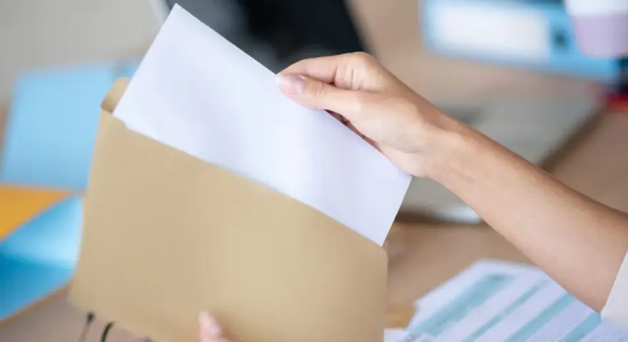 Dłoń wkłada biały papier do brązowej koperty. Wzór adresowania koperty A4 jest gotowy do wypełnienia.