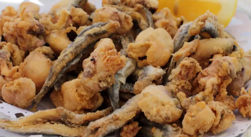 Frito y crujiente pescado en adobo, con trocitos de calamar y una rodaja de limón.