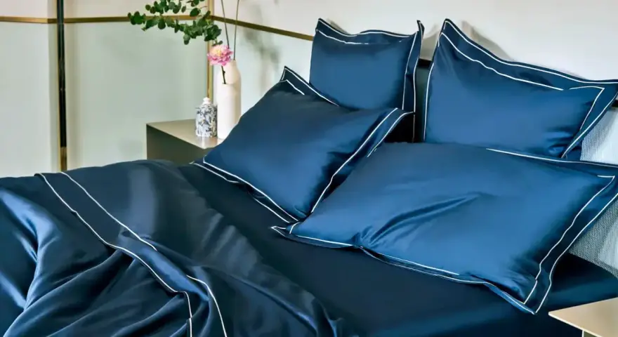 Letto matrimoniale con copriletto blu scuro e cuscini coordinati, rifiniti con bordi bianchi. Ideale per conoscere le misure copriletto matrimoniale.