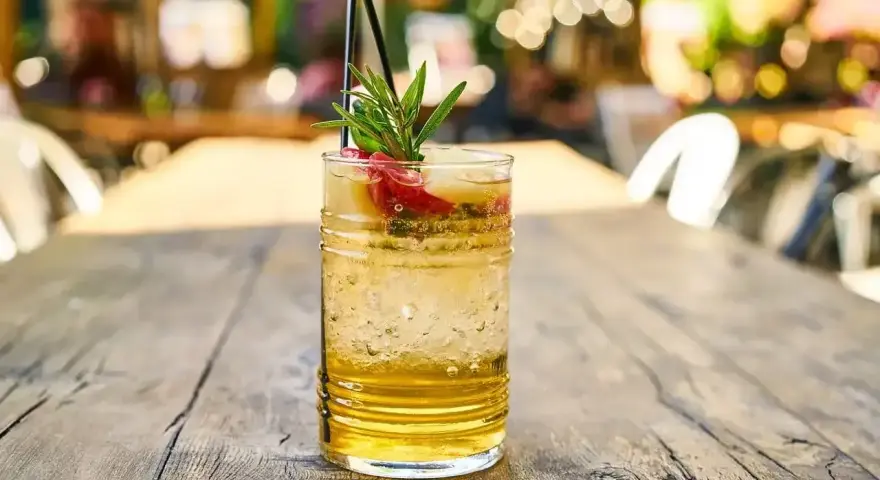 Orzeźwiający drink z plasterkami owoców i gałązką rozmarynu, idealny na letnie popołudnie. W szklance widać bąbelki, sugerujące, że to piwo gingers.