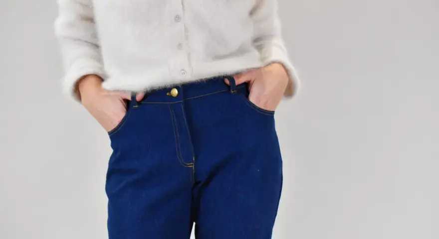 Gros plan sur une personne portant un pull blanc et un pantalon en jean bleu avec les mains dans les poches.